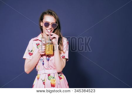Beautiful Woman In Dress With Printed Friuts Posing With Glass Of Fresh Friut Drink On Blue Backgrou