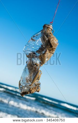 closeup of a used plastic bottle, covered with wet sand, in a fish hook, freshly fished in the ocean