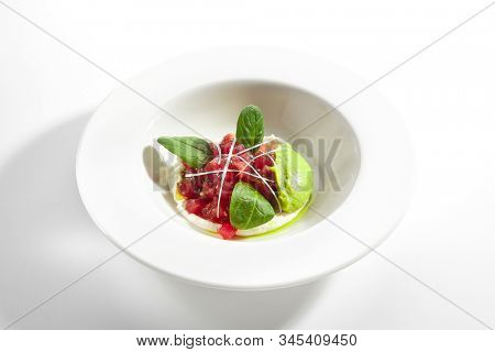 Gourmet tuna tartar with various dip and vegetables on white restaurant plate isolated. Macro shot of raw yellowfin fish tatar, luxury healthy food, seafood with cream sauce and spinach closeup