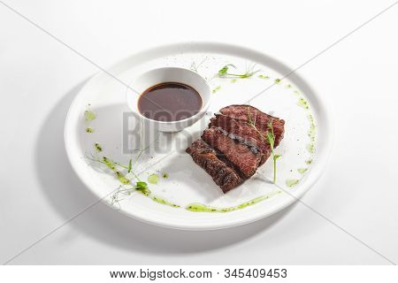 Alternative grilled skirt steak, well done machete fillet on white restaurant plate isolated. Side view of fresh juicy beef grillsteak, barbecue meat with brown spicy sauce and herbs