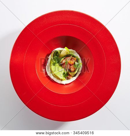 Gourmet salmon tartar with avocado puree, fresh parsley, lemon, spices on red restaurant plate. Top view of delicious luxury raw trout, tuna or yellowfin tatar above