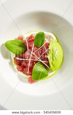 Gourmet tuna tartar with various dip and vegetables on white restaurant plate isolated. Top view of raw yellowfin fish tatar, luxury healthy food, seafood with cream sauce and spinach above
