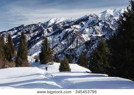 Hiker Is Walking On The Winter Trail Against Spectacular Mountains And Blue Sky Background
