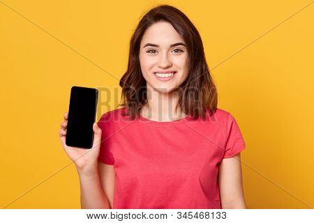 Horizontalshot Of Young Woman Showing Her Mobile Cell Phone With Black Screen Over Yellow Background