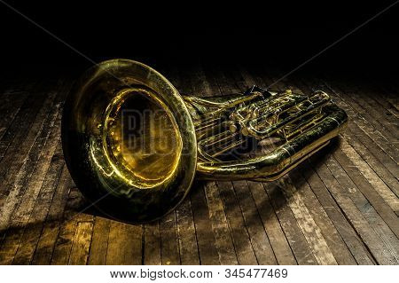Golden Brass Wind Instrument Euphonium Lies On A Brown Wooden Stage In The Light Of A Spotlight