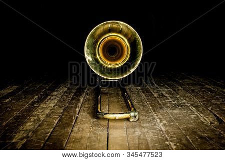 Yellow Brass Instrument Trombone Lies On The Wooden Floor Of The Stage. Front View On The Bell