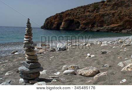 Closeup Of Pyramid Of Stones On Sandy Beack Background Of Blue Sea, Coastline And Rocky Mount
