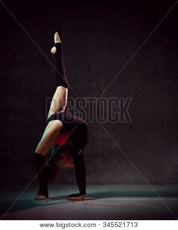 Young Smiling Girl Gymnast In Black Sport Body And Uppers Standing In Bridge Pose And Holding Pink G