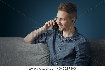 Relaxed Smiling Young Man Talking On The Phone Sitting On Sofa