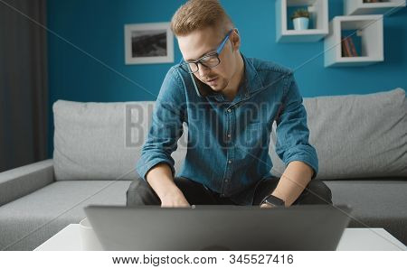 Male In Glasses Talking On Smartphone Holding It With Shoulder While Working On Laptop Sitting At Co