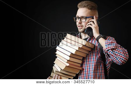 Busy Student In Glasses With Huge Pile Of Books Talking Cellphone Isolated On Black Background