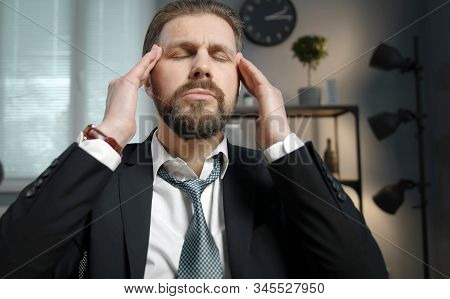 Tired Businessman Sitting With Closed Eyes And Massaging His Temples With Both Hands In Office