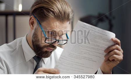 Close-up Of Astonished Bearded Businessman Wearing Glasses Reading Document With Wide Open Eyes At W