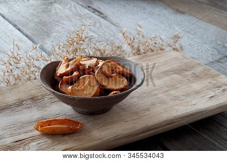 Dried Apple Slices In A Ceramic Plate Stand On A Textured Wooden Board, Next To A Dried Apple In The