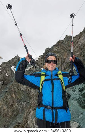 Female Mountaineer Celebrating Ascend With Walking Poles Raised High.