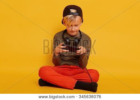 Portrait Of Boy, Playing Online Video Games Via His Modern Smartphone Isolated Over Yellow Backgroun