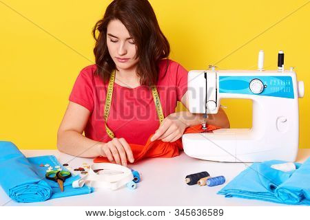 Indoor Shot F Concentraed Woman Dressmaker Sewing In Her Studio, Sitting With Opened Mouth, Ready To
