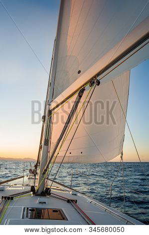Chasing The Sun At Sailing Yacht. Deck And Sails Of Sailoat Pointing To The Sunrise. Mediterranean S
