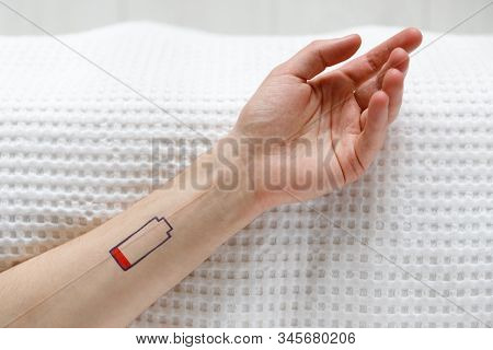 Low Battery Symbol Drawn On Human Hand. Tired Man Lying On The Bed, Top View. Overwork, Exhausted, C