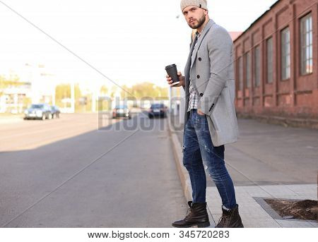 Handsome Young Man In Grey Coat And Hat Crossing The Street With A Cup Of Coffee.