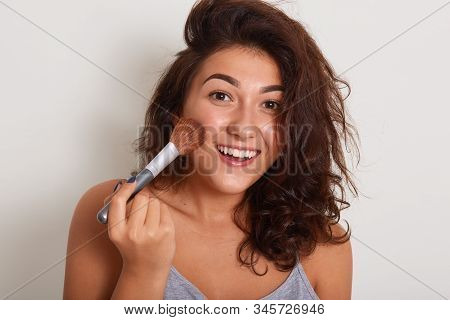 Horizontal Studio Shot Of Beauty Blogger Recording Makeup Tutorial, Smiling Sincerely, Applying Blus