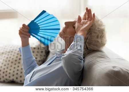 Exhausted Older Woman Feeling Unwell, Suffering From Heat, Waving Fan