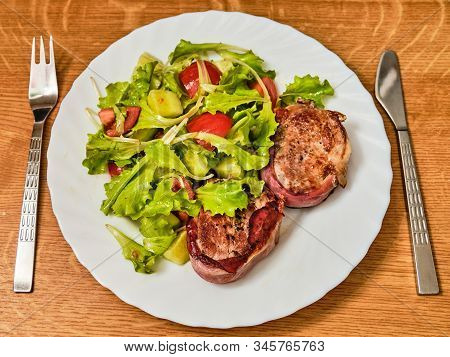 Tasty Pork Tenderloin Meat Steak In Dried Ham With Salad With Sloced Tomato And Cucumber On White Pl