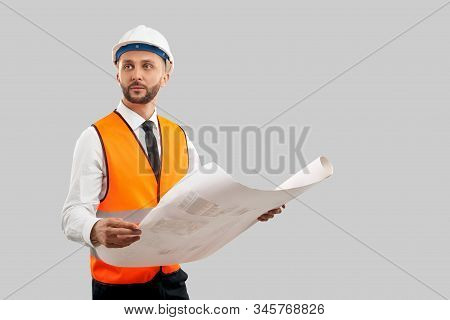 Front View Of Young Bearded Architect In Orange Reflective Vest And Helmet Holding Big Map. Engineer