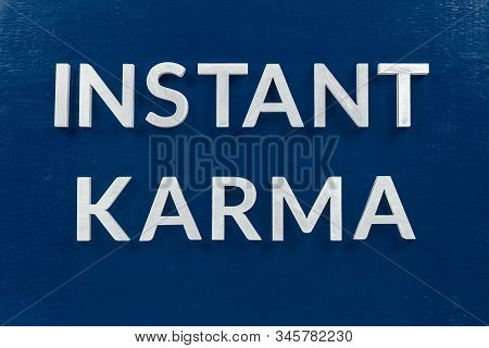 The Phrase Instant Karma Laid With Silver Metal Letters On Classic Blue Painted Board Background
