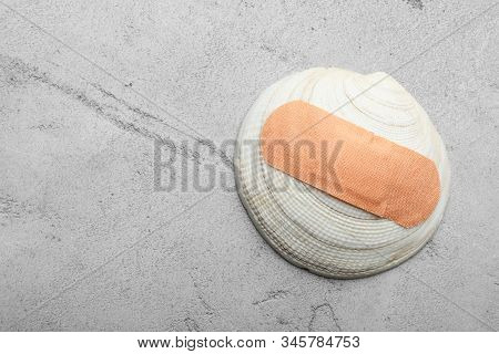 Shell With Sticking Plaster On Light Grey Stone Table, Top View. Space For Text