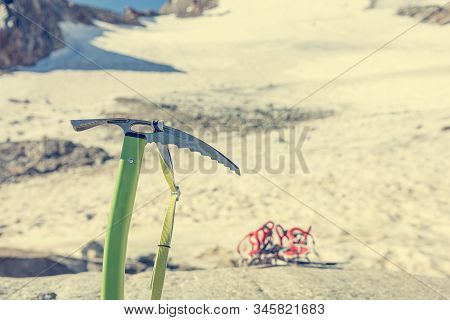 Ice Axe Positioned In Snow With Crampoons In The Background.
