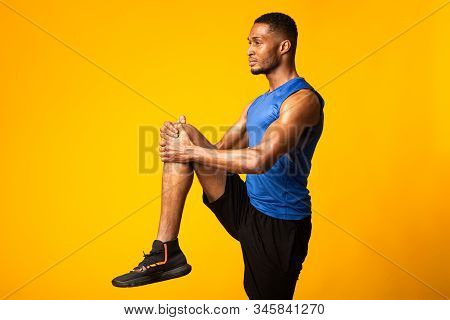 Warm Up. Side View Of Afro Man Doing High Knees Exercise, Lifting Leg Over Yellow Background, Copysp