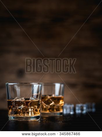 Whisky, Whiskey, Bourbon Or Cognac With Ice Cudes On Black Stone Table And Wood Background