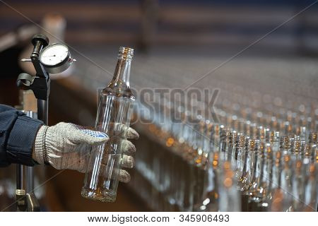 Glassworks. Glass Industry. Working Hands Hold A Glass Bottle On The Background Of A Conveyor Belt.