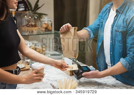 Barista Man Standing Behind The Bar Sells Food And Drink To Woman Client For Takeaway