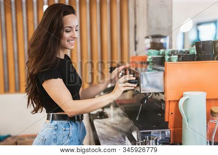 Young Smiling Barista Woman Working Behind The Bar, Stands Near Professional Coffee Machine