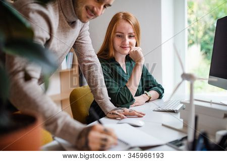 Architects With Computer Sitting At The Desk Indoors In Office, Working.