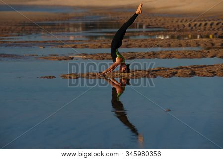 Yoga Headstand Variation Sea Background. A woman performing a headstand on beach in the sea