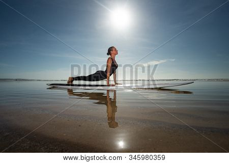 A woman performing a yoga asana Bhujangasana - ÃÂ¡obra pose on a longboard in the sea