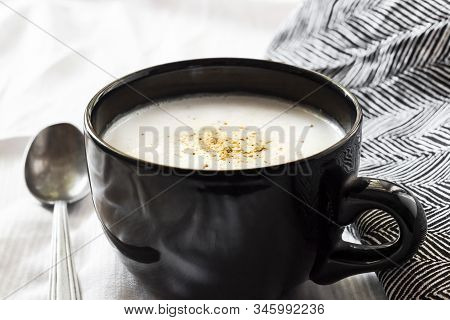 Cauliflower Soup (creme Du Barry) In Black Bowl On White Background With Black And White Cloth.