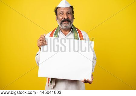 Portrait Of Happy Smiling Indian Poliician Holding Empty White Sign Board By Looking At Camera On Ye