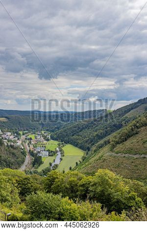 Aerial View, Town Of Bourscheid With Its Houses, A Rural Road And A River Between Mountains Covered 