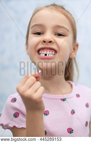 Girl Child Shows A Mouth Without One Missing Milk Tooth. The Girl Holds A Fallen Milk Tooth In Her H