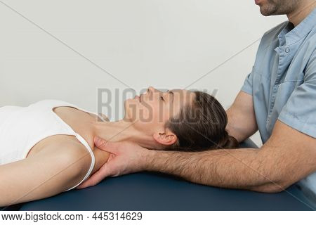 Female Patient Receiving Osteopathic Neck And Shoulder Treatment. Therapist Manipulating Back Of Hea