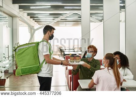 Male Employee Taking Pizza And Coffee From Courrier During Break With Multiethnic Female Colleagues 