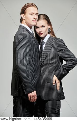 Fashion shoot. Portrait of stylish young man and woman in elegant striped pantsuits posing on a gray background. Impeccable look. Men's clothing style. 