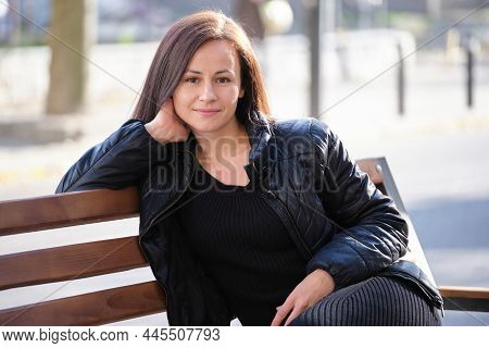 Young Happy Woman Sitting Relaxed On Street Bench On Warm Autunm Day. Wellness And Resting From Ever