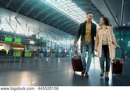 Beautiful Couple In Love Smiles, Laughs, Enjoys A Joint Journey, Walks Through The Departure-arrival