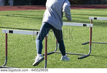 Rear View Of A High School Hurdle Runner Perfoeming The Trail Leg Drill On A Turf Field.