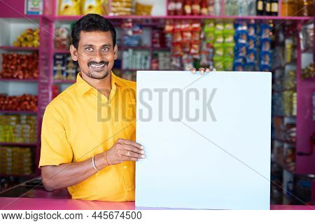 Kirana Or Groceries Merchant Or Shopkeeper With Empty Sign Borad Looking At Camera - Concept Of Adve